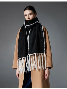 Dettaglio di sciarpa nera in maglia con cuciture bianche a contrasto e nappe su cappotto