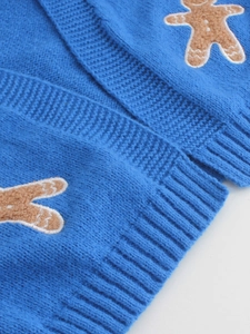 Close-up of blue knit sweater with embroidered gingerbread man patch and ribbed hem detail