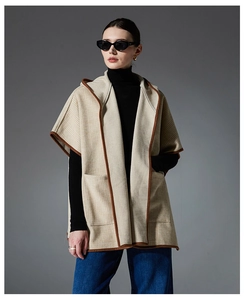 Detail of beige plaid hooded poncho featuring large pockets and dark brown trim accents