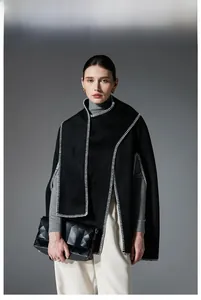 Close-up of black sleeveless cape with white hand-stitched edges and elegant hand bag
