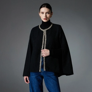 Women's black tweed cape jacket with gold trim paired with high-neck knitwear and jeans