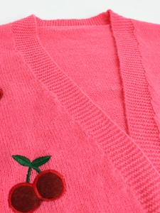 Detailed close-up of vibrant pink knit cardigan with red cherry embroidery and V-neckline