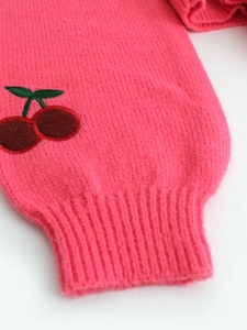 Detail of pink knit sweater cuff with red cherry embroidery and ribbed sleeve texture