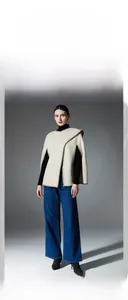 Detail of beige knit poncho featuring black contrast stitching and halter neck design