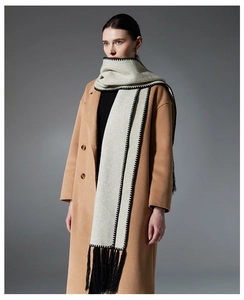 Detail of cream knit scarf featuring black contrast stitching and long tassel trim