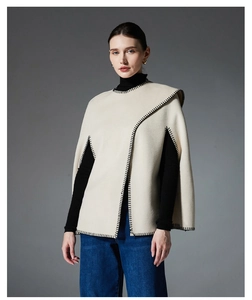 Chic cream-colored poncho cape with black whipstitch edges styled over a black turtleneck