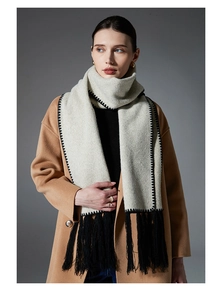 Detail of beige winter scarf with black hand-stitched edges and long tassel fringe