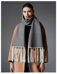 Dettaglio sciarpa invernale grigia con nappe bianche su un cappotto beige
