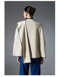 Detail of beige sleeveless poncho cape with black contrast blanket stitch edging