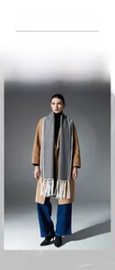 Grey double-sided wool scarf with white tassel trim worn over a camel wool coat