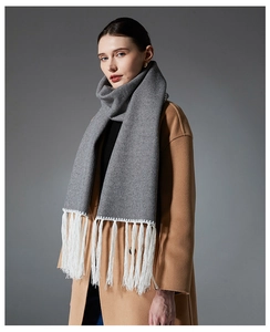 Detail of gray wool scarf featuring contrast white fringe tassels on camel winter coat
