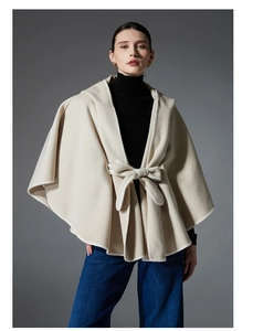 Detail of beige hooded cape with front bow tie closure and refined piped edges