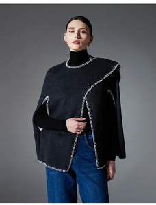 Detail of grey knitted poncho featuring contrast white whipstitch edges and premium texture