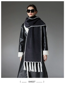 Detail of solid black scarf with white wave embroidery and long tassels on wool fabric