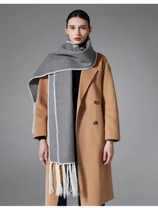 Detail of grey winter scarf with long white tassels and lock-stitched edges on camel coat