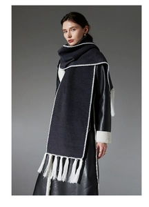 Detail view of black wool scarf with white wavy stitched edges and long fringe tassels
