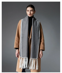 Detail of grey winter scarf with white V-stitching and long fringe on a wool coat