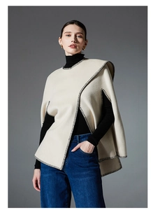 Detail of off-white poncho cape showing black blanket stitch embroidery and premium fabric