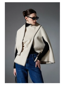 Detail of off-white poncho cape with black contrast stitching on the edges and hemline