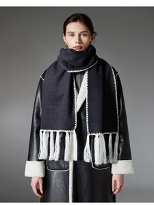 Detail of dark grey scarf with white contrast stitching and long tassels on black coat