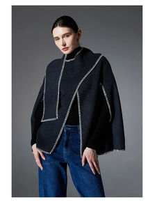 Detail of dark grey knitted poncho featuring decorative white blanket stitch edging