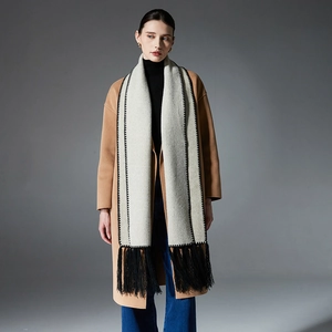 Elegant beige wool-like scarf with black stitch embroidery and tassels on a model