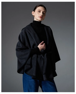Detail shot of a dark grey hooded wool cape coat showing premium fabric and elegant drape