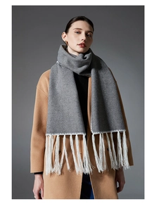 Detail of dark grey scarf with white fringe and zigzag stitching on camel coat