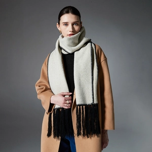 Sciarpa invernale beige con nappe nere e cuciture a contrasto su un cappotto beige
