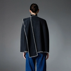 Minimalist black wool cape coat with white contrast whipstitch seams on model back view