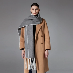 Elegant grey long winter scarf with white stitching and tassels on a camel wool coat