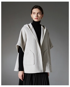 Détail d'une cape en laine gris clair à capuche avec passepoil blanc et grandes poches