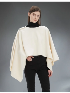 Dettaglio della mantella crema con bottoni argentati e taglio asimmetrico elegante