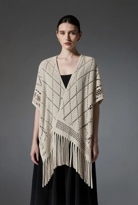 Détail d'un châle beige en tricot ajouré avec motifs géométriques et longues franges
