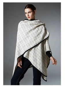 Detail of checkered knit poncho featuring ivory white fabric and wide black border trim