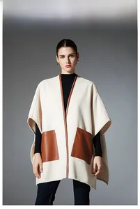 Detail of cream cape coat featuring brown leather-trimmed pockets and elegant stitching