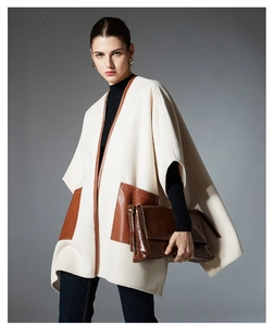 Detail of cream-colored cape with brown leather trim and large contrast pockets