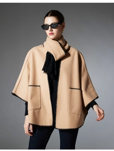 Detail of camel wool poncho coat featuring black whipstitch edging and matching fringe scarf