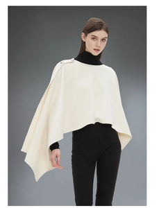 Dettaglio del poncho bianco crema con eleganti bottoni argentati sulla spalla