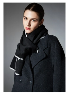 Detail shot of solid black scarf featuring white zigzag embroidery and heavy wool texture