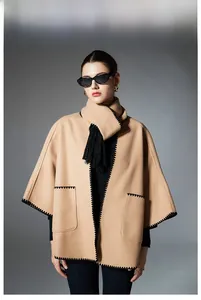 Detail of camel wool cape coat featuring black blanket stitching and scarf with tassels