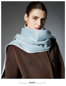 Detail of light blue textured scarf with white edge stitching on brown wool coat