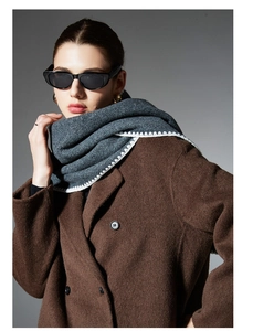 Detail of grey knitted scarf with white sawtooth embroidery worn with a wool coat