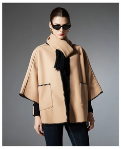 Detail of camel wool cape showing black whipstitch edges and long fringe tassels