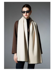 Detail of cream whipstitch scarf with black edges paired with a brown wool coat