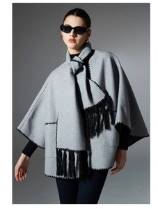 Detail of grey knitted shawl showing black zigzag stitching and long tassel fringe trim