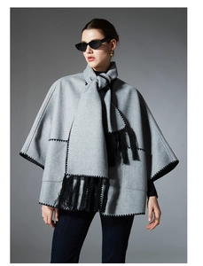 Detail of grey poncho shawl with black wave stitching and long tassels for autumn winter