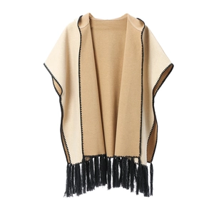 Elegant beige and camel knit poncho with black fringe trim and decorative stitching