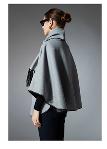 Detail of grey cape shawl featuring black scalloped embroidery and decorative tassels