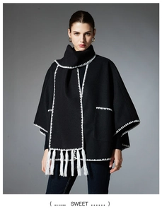 Detail of grey poncho scarf with white geometric embroidery and long tassels on edges